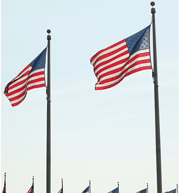 Two American flags waving against blue sky.